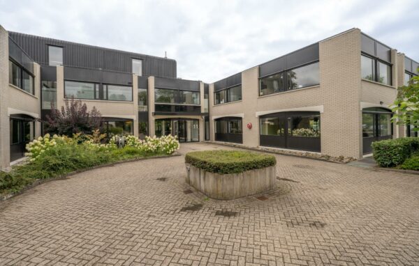 Moderne kantoor- of zorginstelling aan de Burgemeester Verderlaan met een betegelde binnenplaats en bloeiende beplanting.